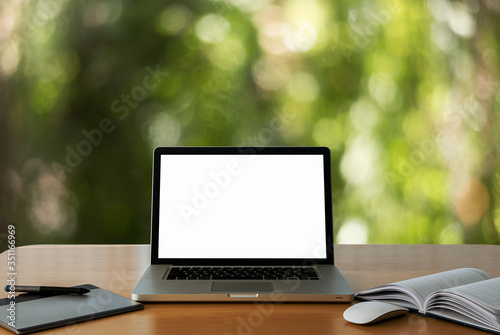 laptop showing blank screen a wooden table at nature bokeh background.