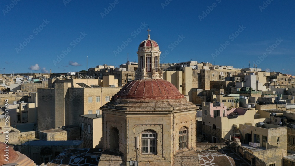 Aerial view of dome of the church against the backdrop of the city, historical architecture. Roof tops. Bormla, Valletta, Malta. Travel destinations. European culture and religion.
