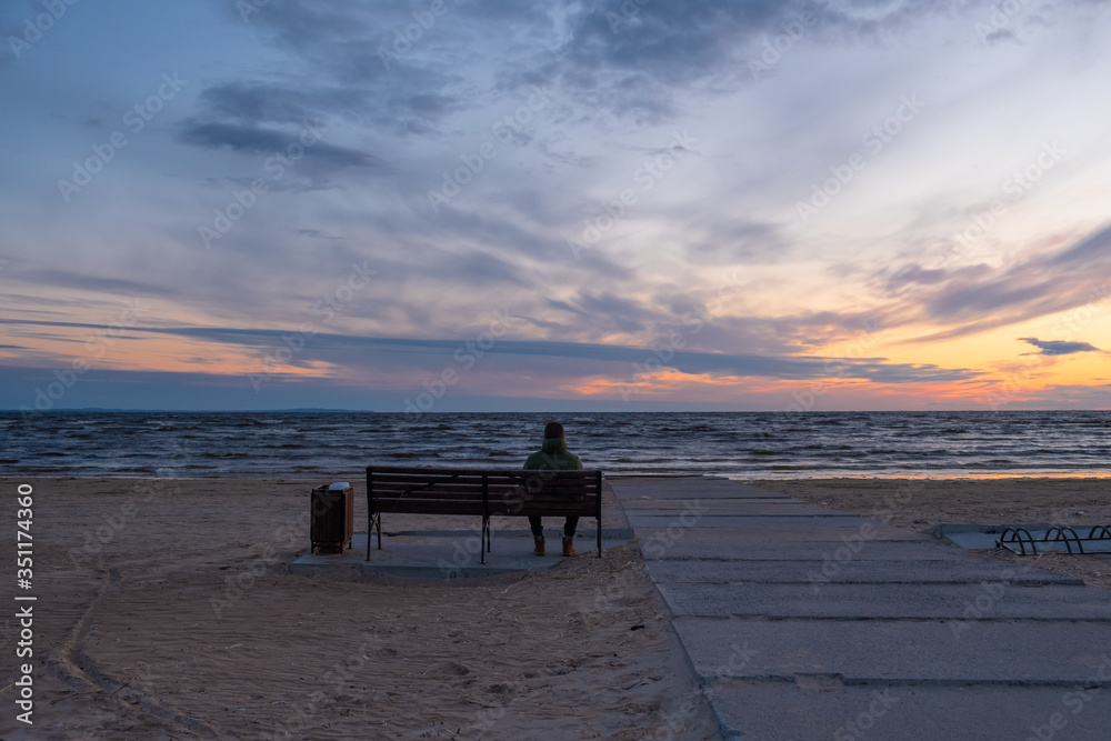 A man sits on a bench near the sea