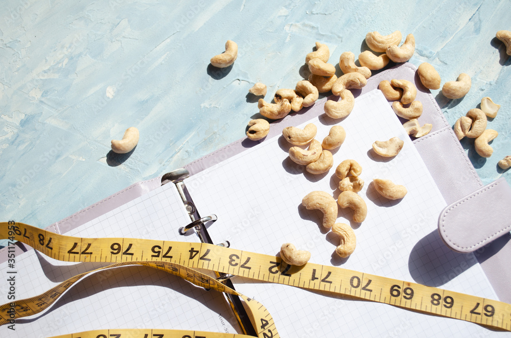 
Notepad and yellow measuring tape and cashews lie on a blue background. concept diet. Healthy snack concept.