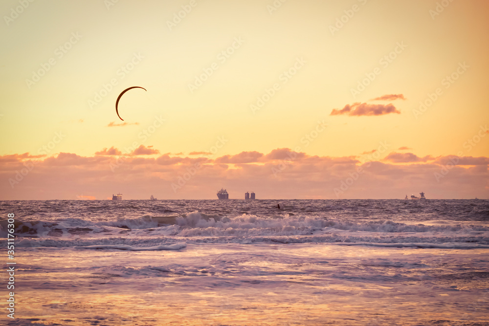 Extreme Sport Kitesurfing, cargo ships on the horizon. Surfer in the sea at Scheveningen at sunset