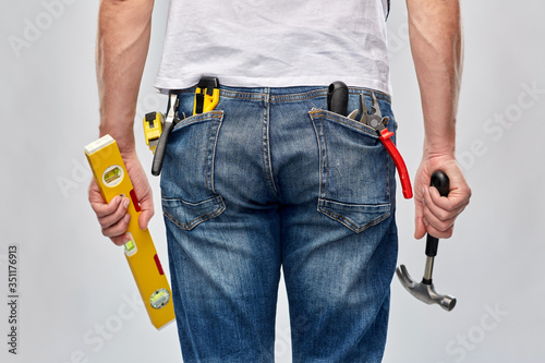 repair, construction and building - male worker or builder with level and working tools in back pockets over grey background photo