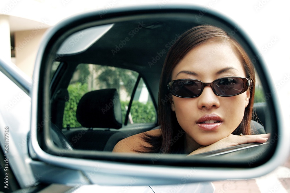 View of woman in sunglasses through the side view mirror of car.