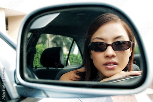 View of woman in sunglasses through the side view mirror of car.
