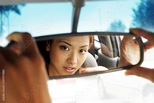 Fotografia Mirror reflection of woman adjusting the rear view mirror of car.