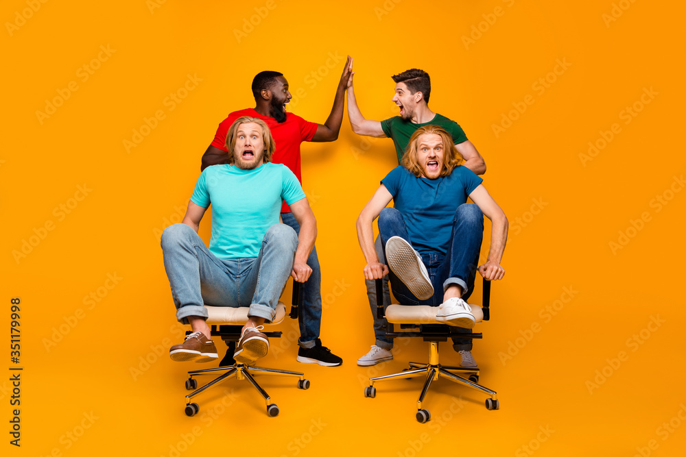 Full size photo two men afro american meeting hold hands high five gesture persuade blonde hair pals office chair ride race scared fast speed isolated yellow color background Full size photo two men afro american meeting hold hands high five gesture persuade blonde hair pals office chair ride race scared fast speed isolated yellow color background