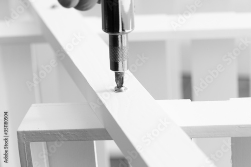 Man assembling a white flat pack ladder shelving unit with a screwdriver.  Flat pack assembly concept photo