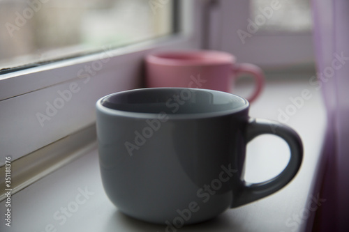 Two empty ceramic mugs of gray and pink on the windowsill.