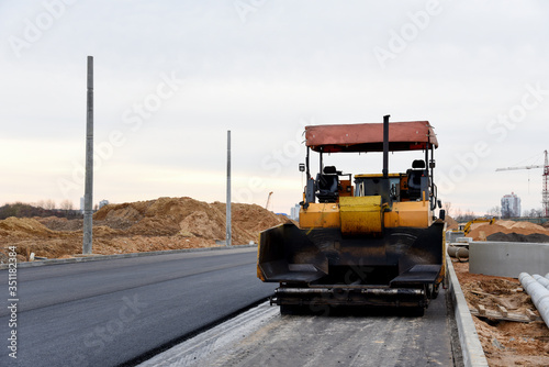 Asphalt paver machine during road work. Road Machinery at construction site for paving works. Screeding the sand for road concreting. Asphalt pavement is layered over concrete pavement. Road Surfacing © MaxSafaniuk