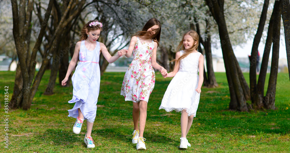 Three beautiful girls in retro dresses for a walk in a flowered garden. The idea and concept of a friendly family and a happy childhood.