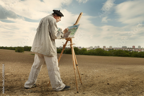 Older man painting artwork on canvas in sunny day field