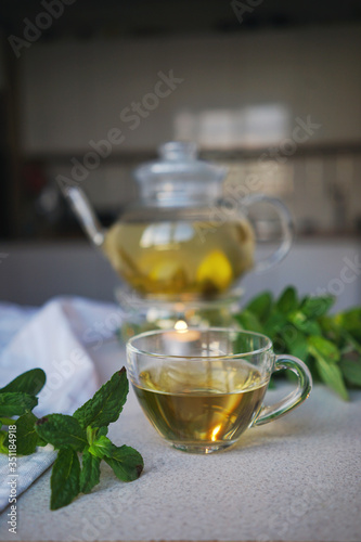  cup with herbal tea on the background of a teapot with sprigs of mint and flowering branches. Tea Party Concept