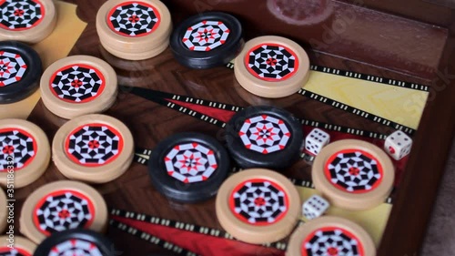 Black and white patterned game chips and dice fall on the playing Board from under the backgammon game