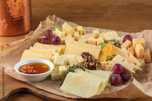 Tasting cheese dish on a wooden plate. Food for wine and romantic, cheese delicatessen on a dark stone table. Top view.