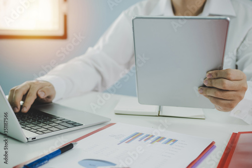 businessman in white shirt working about financial on digital mobile tablet with report document on desk at office, digital marketing, work from home, business finance, network technology concept