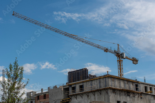 a building under construction and a crane against a blue sky with clouds.