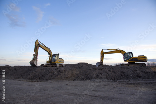 Excavators work at constrruction site on sunset background. Backhoe digs gravel and old concrete. Recycling old asphalt at a landfill for the disposal of construction waste. Construction machinery photo