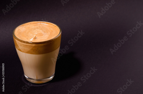 Dalgon coffee in a transparent glass on a dark background. Milk and whipped coffee foam with sugar on top. Korean and indian whipped coffee, copy space, vertical image