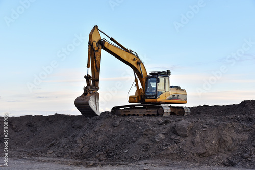 Excavator working on earthmoving at open pit mining on sunset background. Backhoe digs gravel in quarry. Construction machinery for excavation, loading, lifting and hauling of cargo on job sites