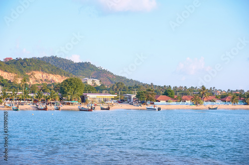 Koh Samui s beach filled with houses  hotels  boats and tourists. A view from the water.
