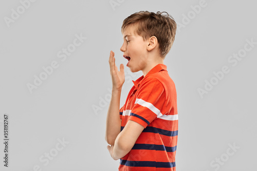 childhood, fashion and people concept - portrait of tired yawning boy in red polo t-shirt over grey background