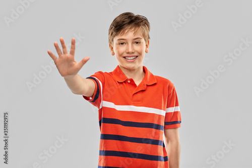 childhood, fashion and people concept - portrait of happy smiling boy in red polo t-shirt showing five fingers over grey background