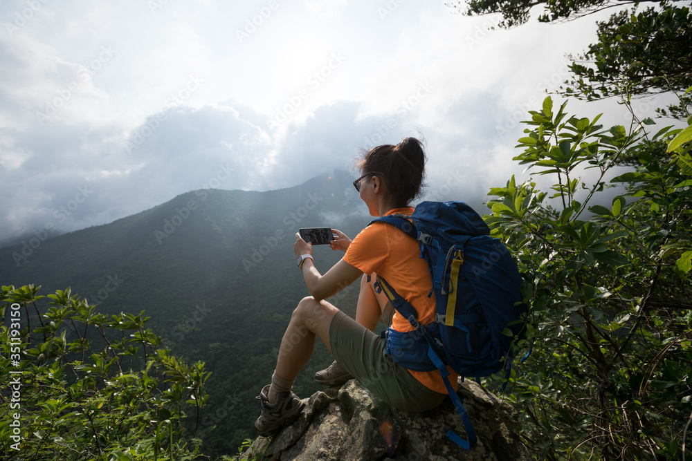 Successful hiker using smartphone on sunrise mountain top cliff edge