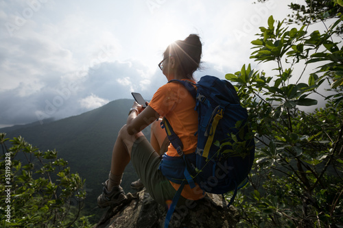 Successful hiker using smartphone on sunrise mountain top cliff edge