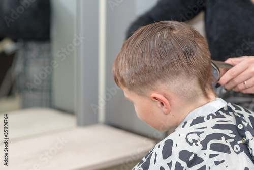 Happy Caucasian boy sits in a barbershop and cuts hair.