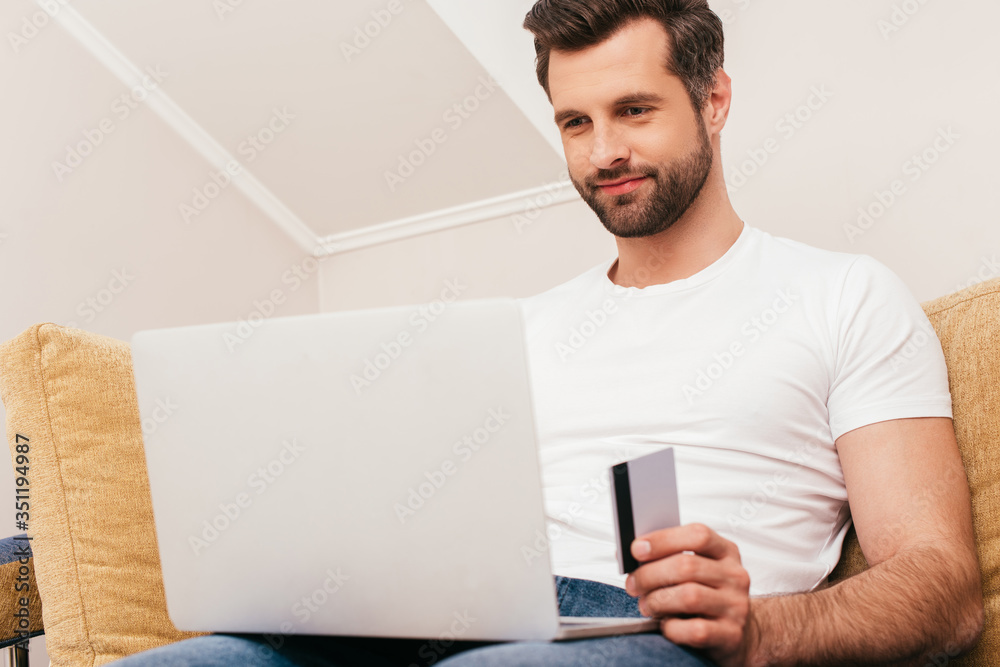 Selective focus of man using laptop and holding credit card at home Selective focus of man using laptop and holding credit card at home