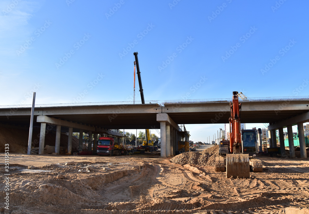 Excavator working at construction highway ramps and bridgeworks. Roundabout and traffic bridge construction. Road work on traffic highway, road intersection junction and freeway. Bridge project works