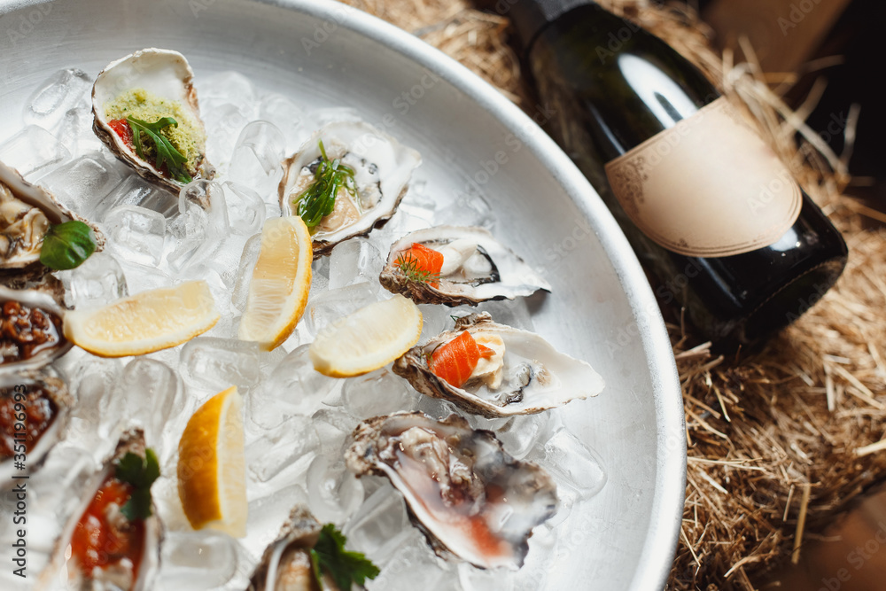 many different oysters lie on ice, a bottle of champagne on a background of hay many different oysters lie on ice, a bottle of champagne on a background of hay