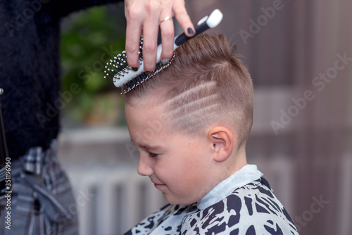 Nice european boy getting hairstyle in barbershop.hairdresser makes a hairstyle for a boy