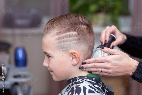 Nice european boy getting hairstyle in barbershop.hairdresser makes a hairstyle for a boy