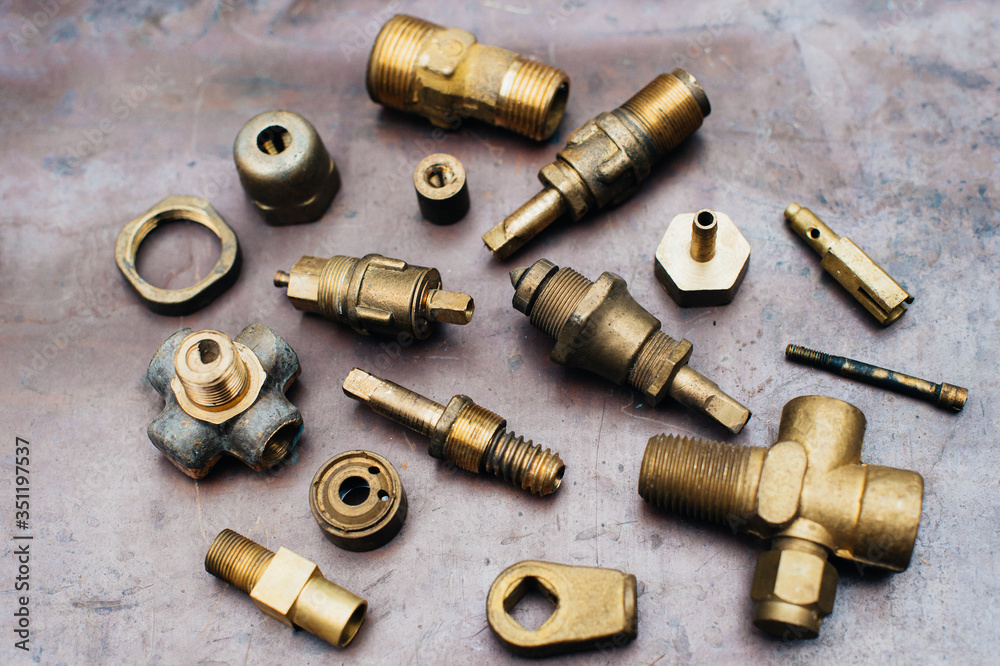 Brass scrap metal: taps, tees, plugs and various plumbing parts, spare parts. Against the background of a copper sheet. Close-up.