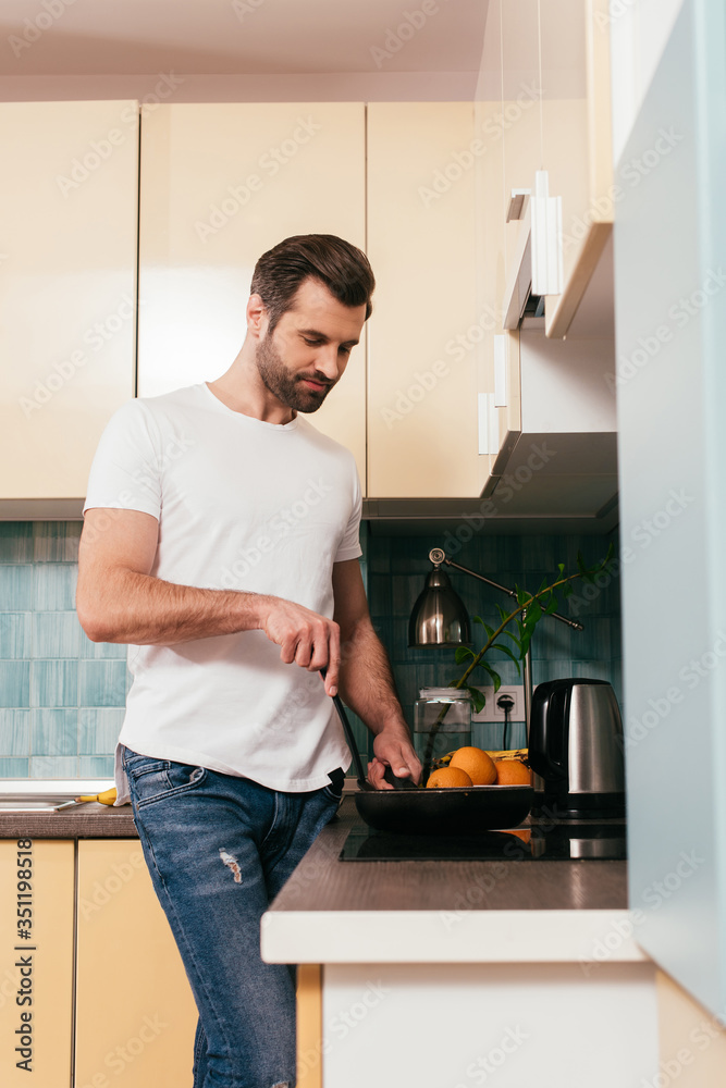 Selective focus of handsome man cooking breakfast in kitchen Selective focus of handsome man cooking breakfast in kitchen