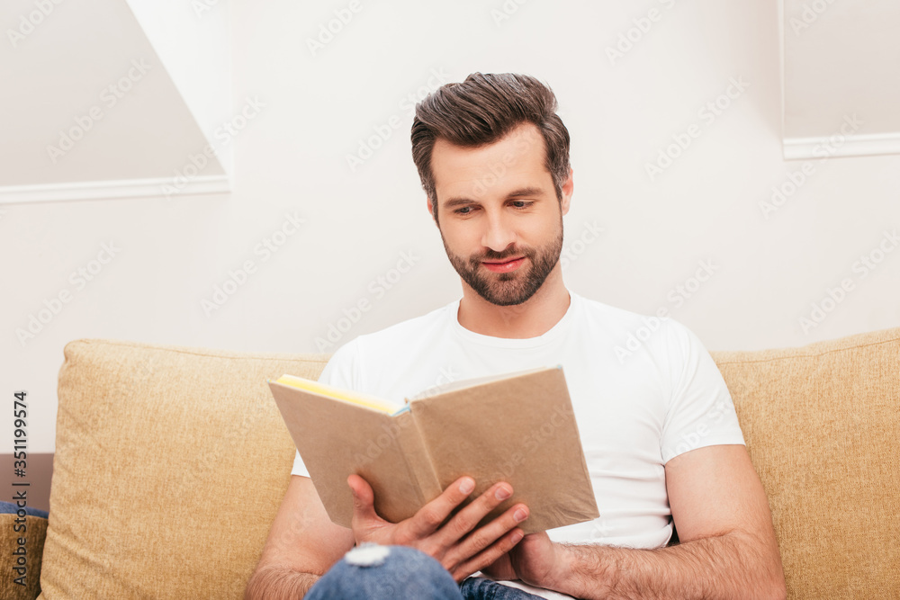 Selective focus of handsome man reading book on couch in living room Selective focus of handsome man reading book on couch in living room