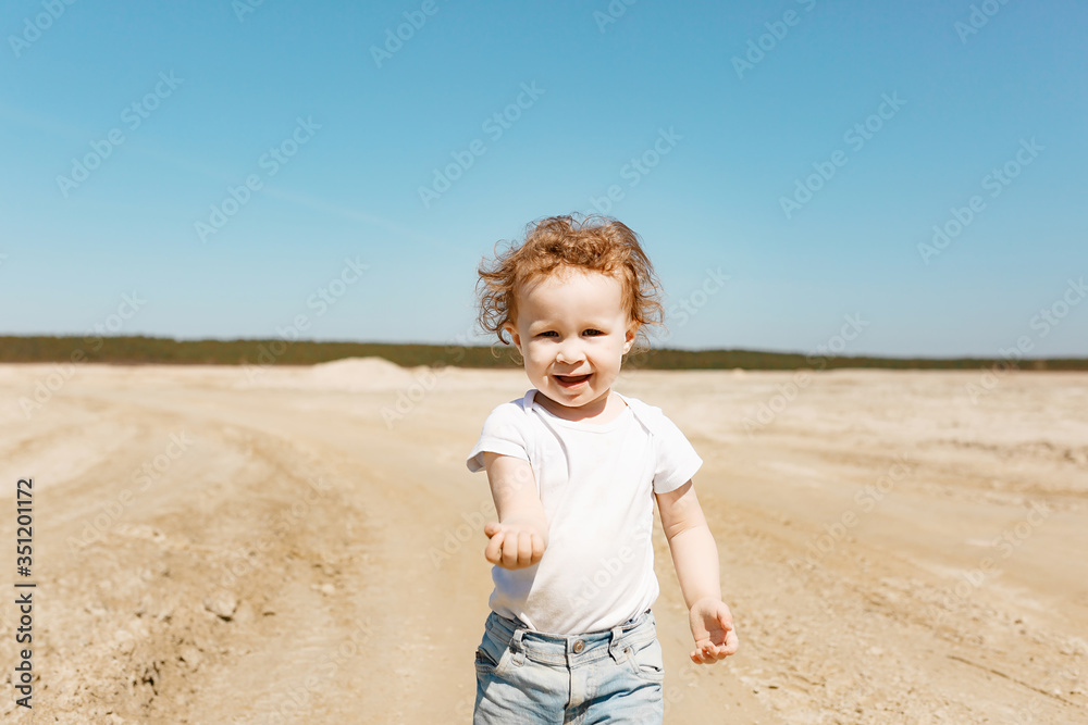 A little girl at the age of 2 walks along the sandy desert in jeans and a white T-shirt. Clear sunny day. A little girl at the age of 2 walks along the sandy desert in jeans and a white T-shirt. Clear sunny day.