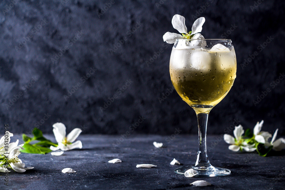 Apple alcoholic cocktail with sparkling wine in glass on a dark background. Refreshing cool summer drink, lemonade or ice tea decorated with apple tree petals. Copy space for text, low key Apple alcoholic cocktail with sparkling wine in glass on a dark background. Refreshing cool summer drink, lemonade or ice tea decorated with apple tree petals. Copy space for text, low key