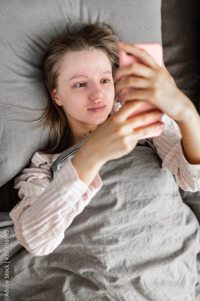 A beautiful woman in sleepwear woke up, smiles and checks the mail on the phone while lying in bed. A beautiful woman in sleepwear woke up, smiles and checks the mail on the phone while lying in bed.