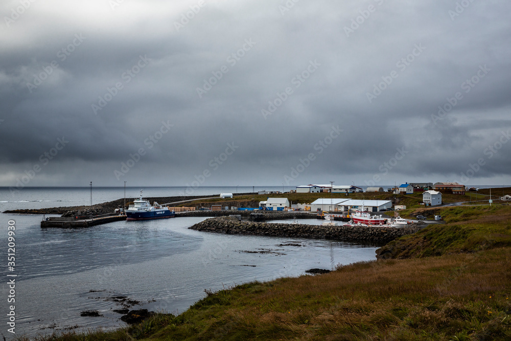 
landscape with the port of the island of grimsey in the north of iceland, off the arctic circle. The sky is loaded with clouds and a moored boat awaits tourists