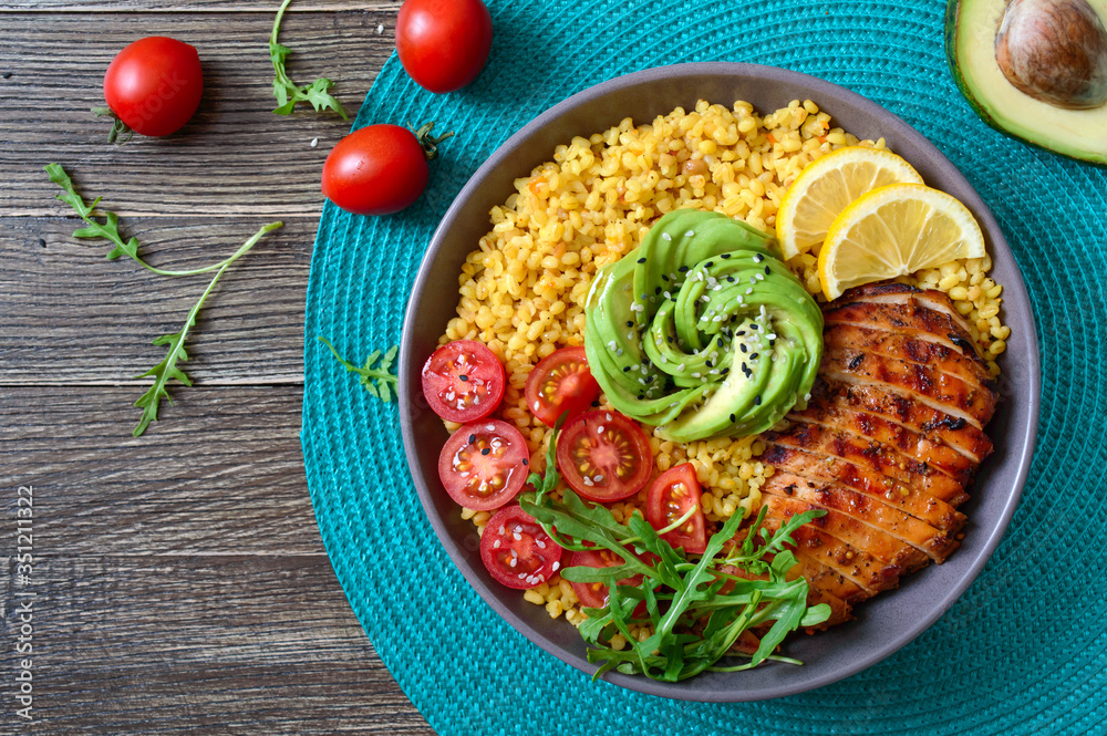 Bulgur with grilled chicken breast, fresh vegetables, avocado, arugula. Diet lunch on a wooden table. Healthy food. Top view.