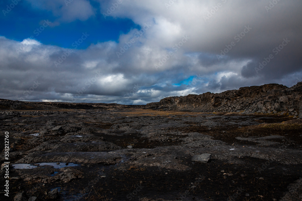 General view of the desert near the Detifoss waterfall in the north of Iceland. The sky is cloudy. The desert is made up of dark volcanic stones covered with greenish moss