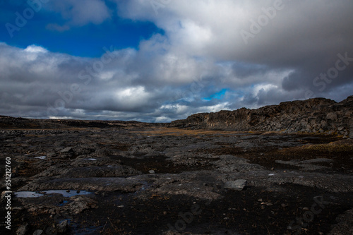 General view of the desert near the Detifoss waterfall in the north of Iceland. The sky is cloudy. The desert is made up of dark volcanic stones covered with greenish moss