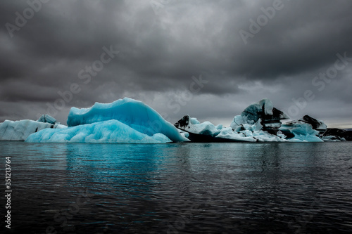 Several glaciers floating in the Jökulsárlón, a glacier lagoon in the south-east of Iceland. They are numerous and have light blue, azure, and white reflections. The sky is gray. photo