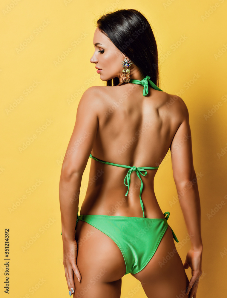 Young tanned slim brunette woman with perfect body in sexy green bikini is  posing back to us Stock Photo | Adobe Stock