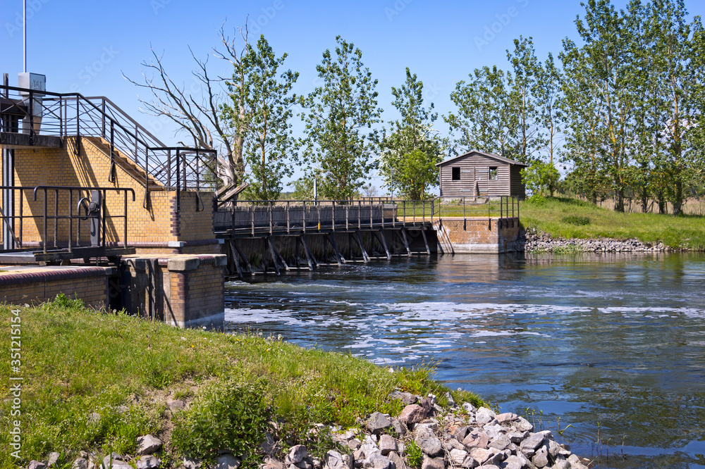 View of an historical weir system. In the background there is a row of poplars.