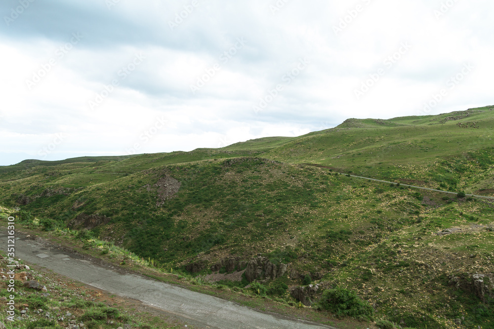 Amazing mountain landscape. Old asphalt road in hilly area near green meadows in cloudy weather Amazing mountain landscape. Old asphalt road in hilly area near green meadows in cloudy weather