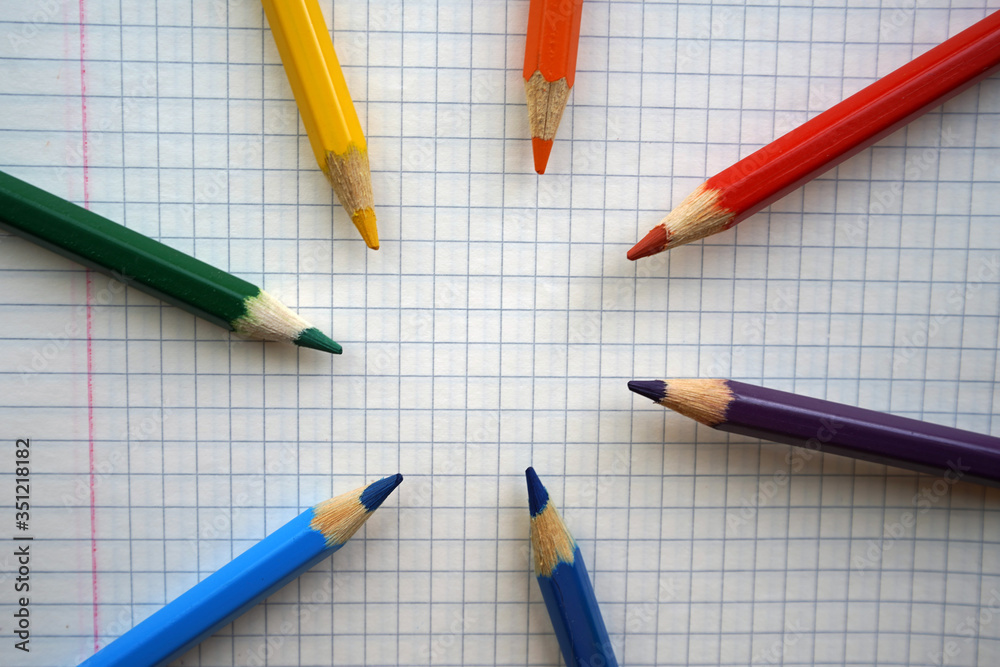 Multi-colored pencils are laid out on a checkered piece of paper, kindergarten, school or copy space for lettering Multi-colored pencils are laid out on a checkered piece of paper, kindergarten, school or copy space for lettering