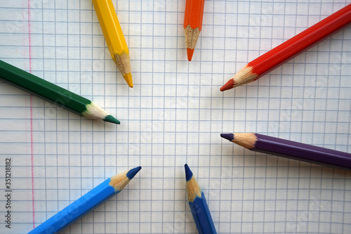 Multi-colored pencils are laid out on a checkered piece of paper, kindergarten, school or copy space for lettering